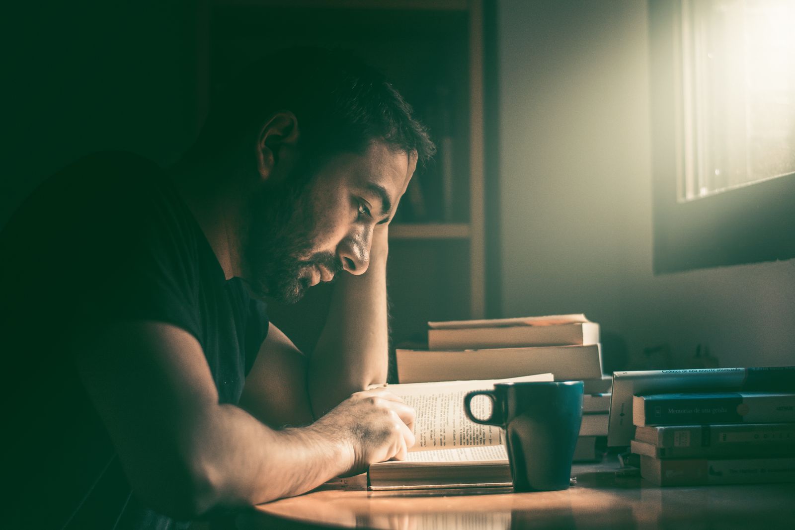 A person reading a book at a desk surrounded by stacks of books