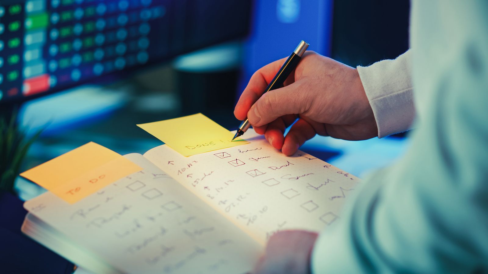 A hand writing in a planner with sticky notes nearby