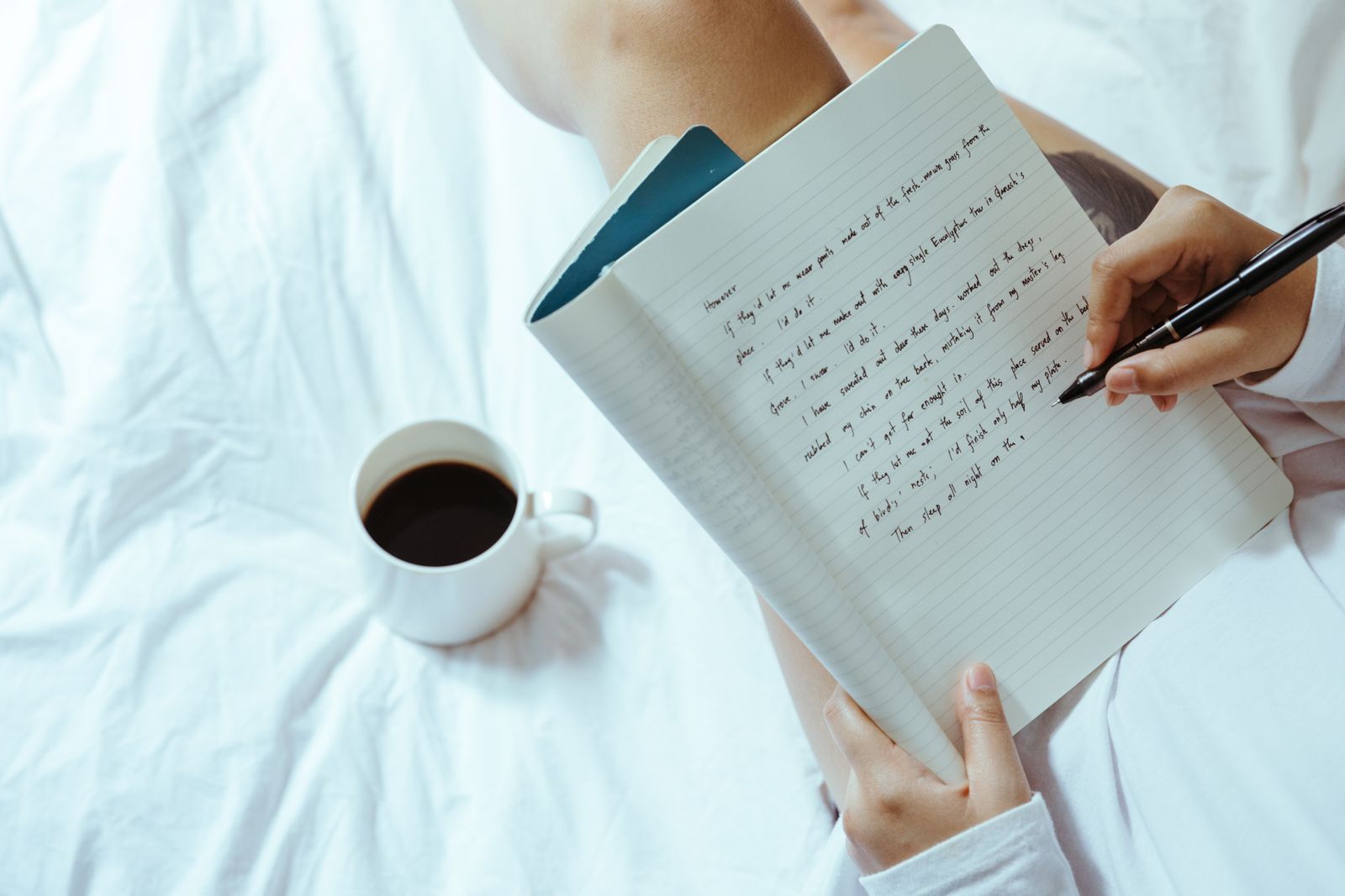 Hands writing notes in a notebook beside a cup of coffee