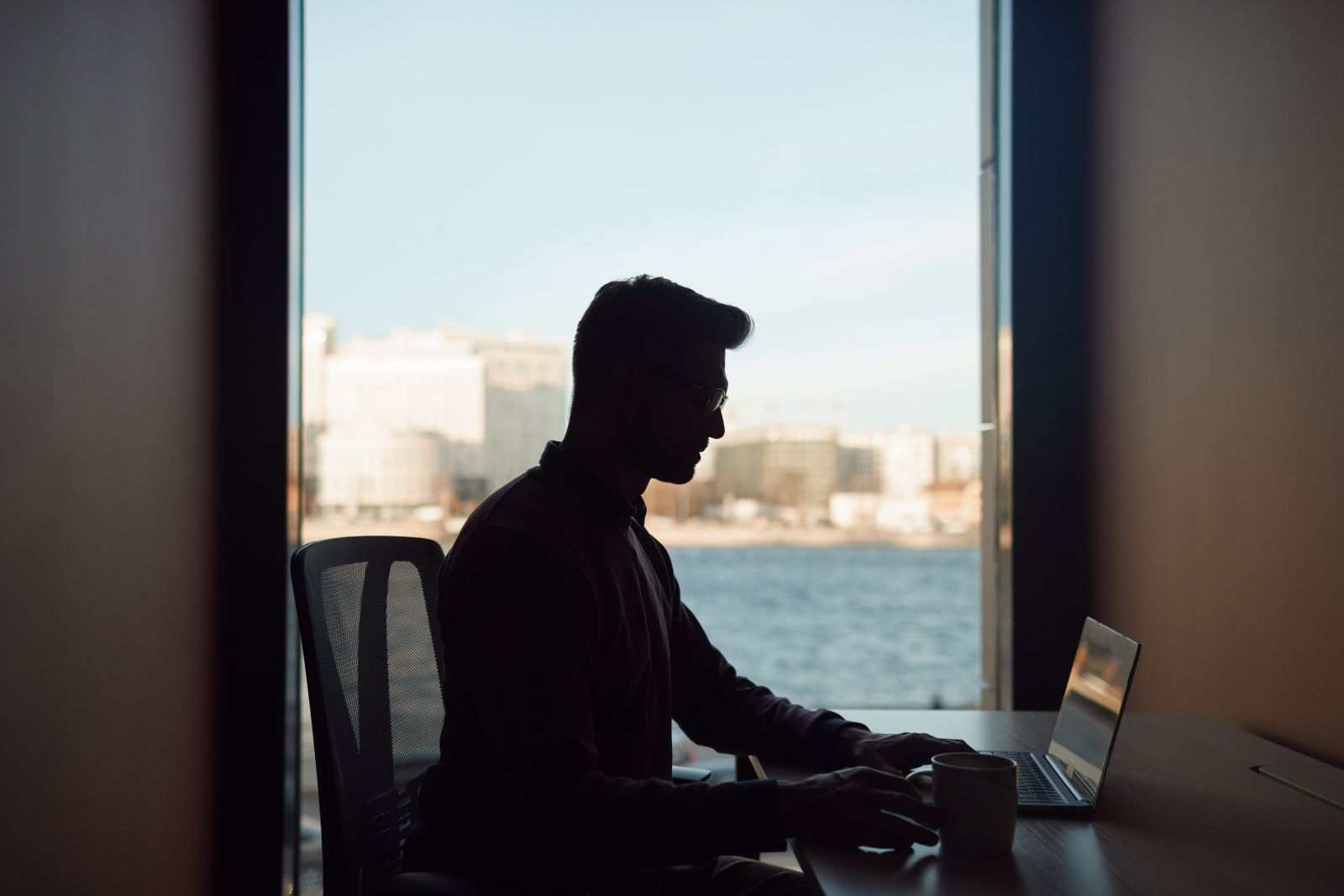 A person working at a laptop by a window in the early morning light
