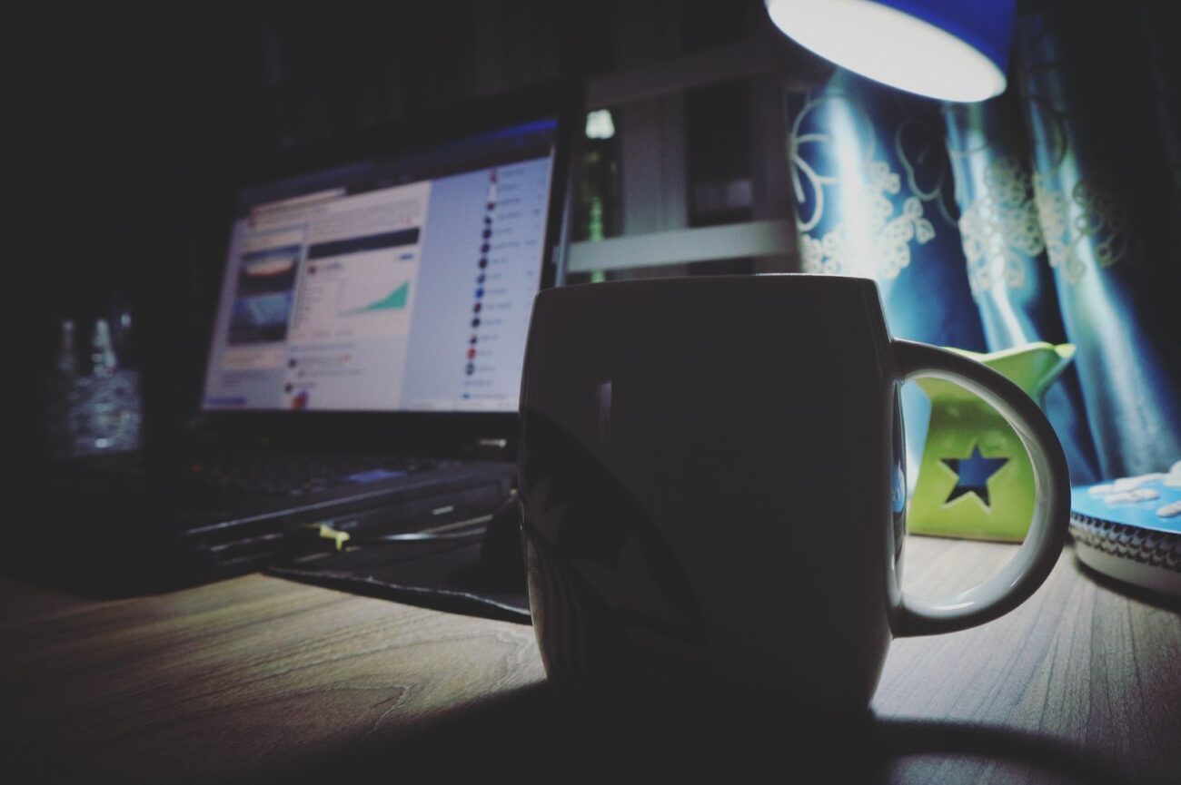 A coffee mug beside a laptop and lamp in the quiet early morning light