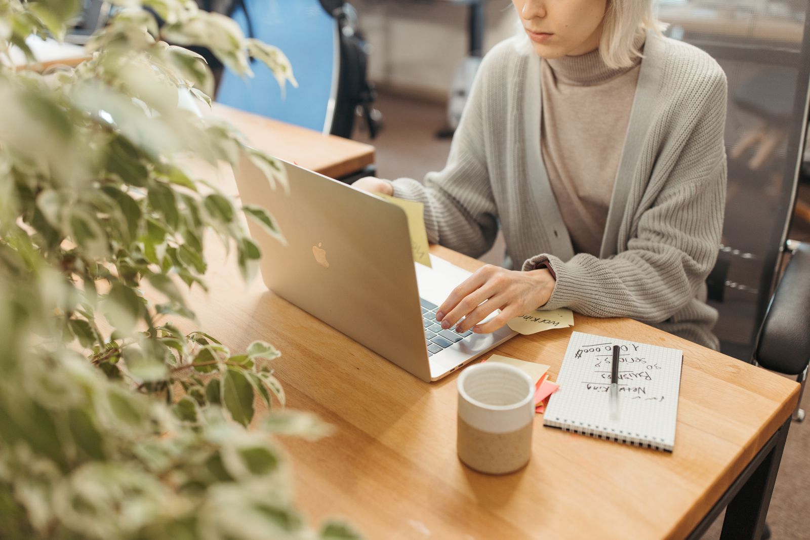 A person working calmly at a laptop with a notebook and coffee
