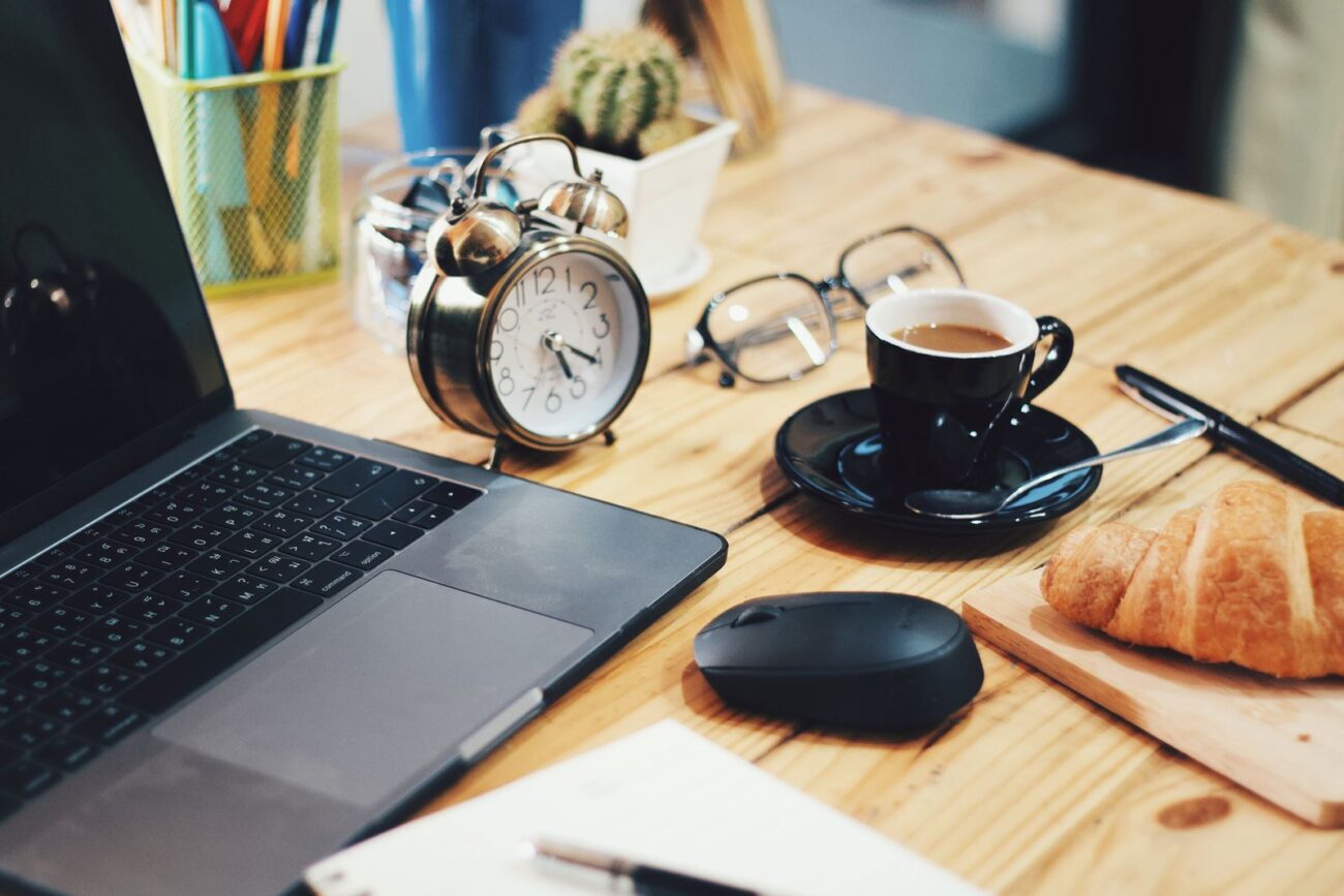 A morning desk with a laptop, alarm clock, and a cup of coffee in bright light