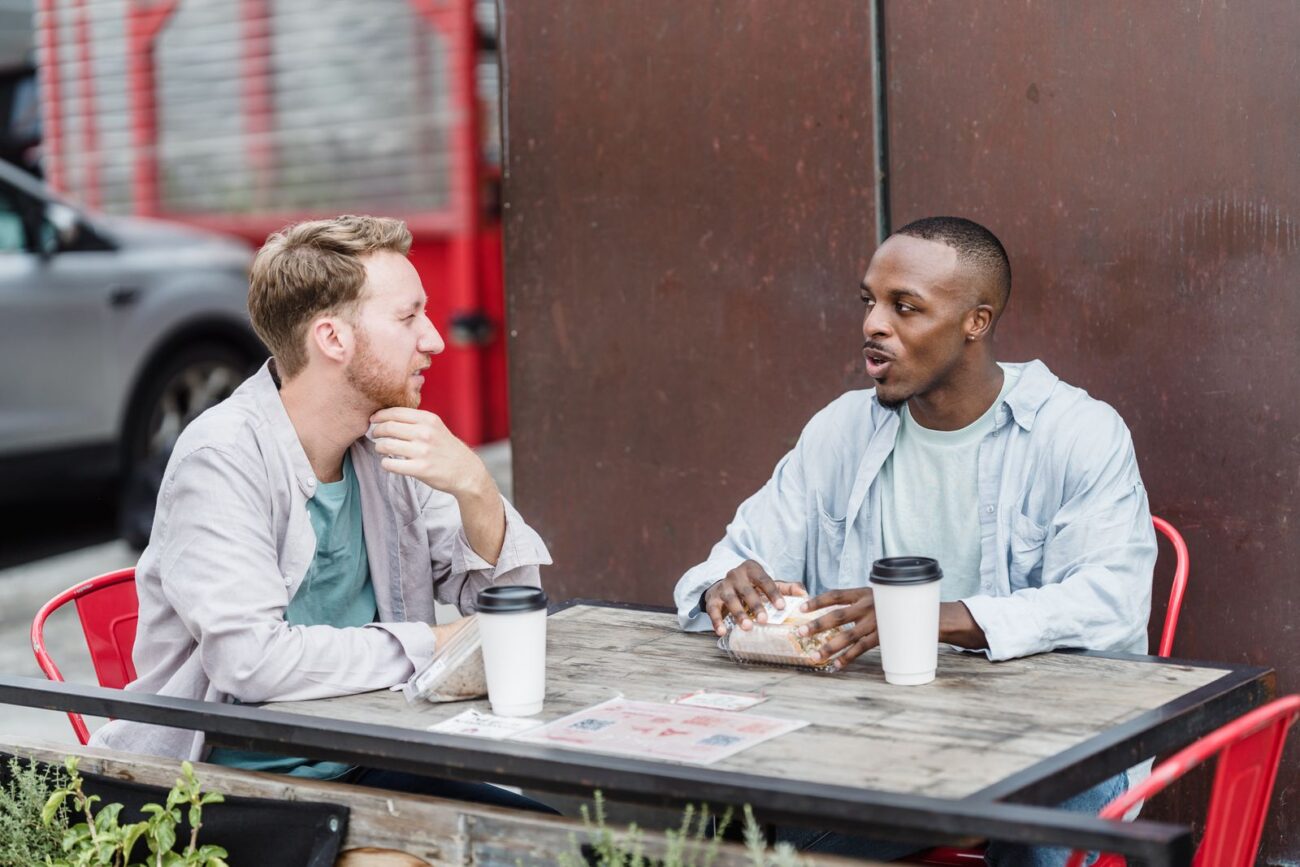 Two adults sitting at a table in conversation, one listening as the other talks