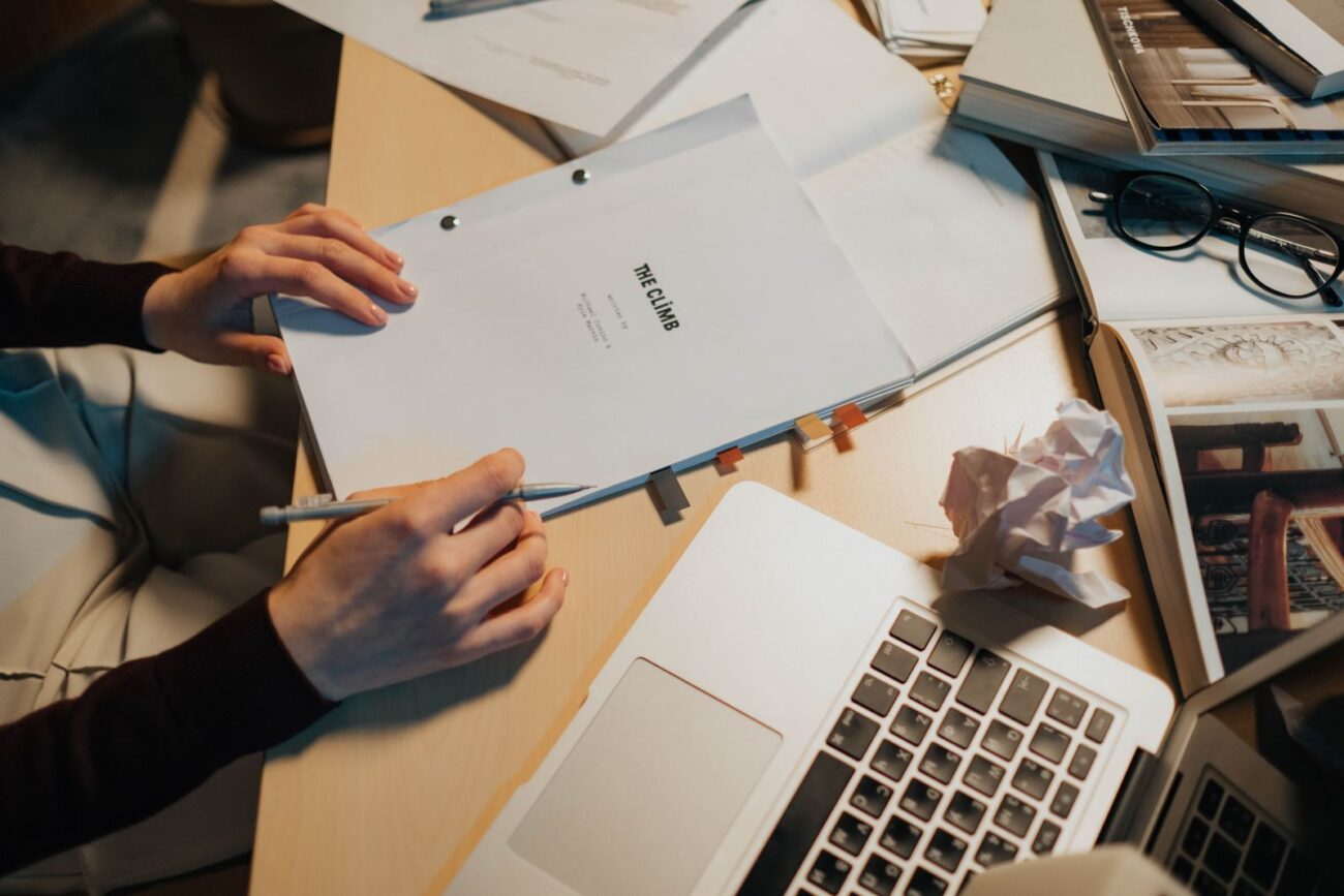 A cluttered desk covered with papers and objects around the actual work