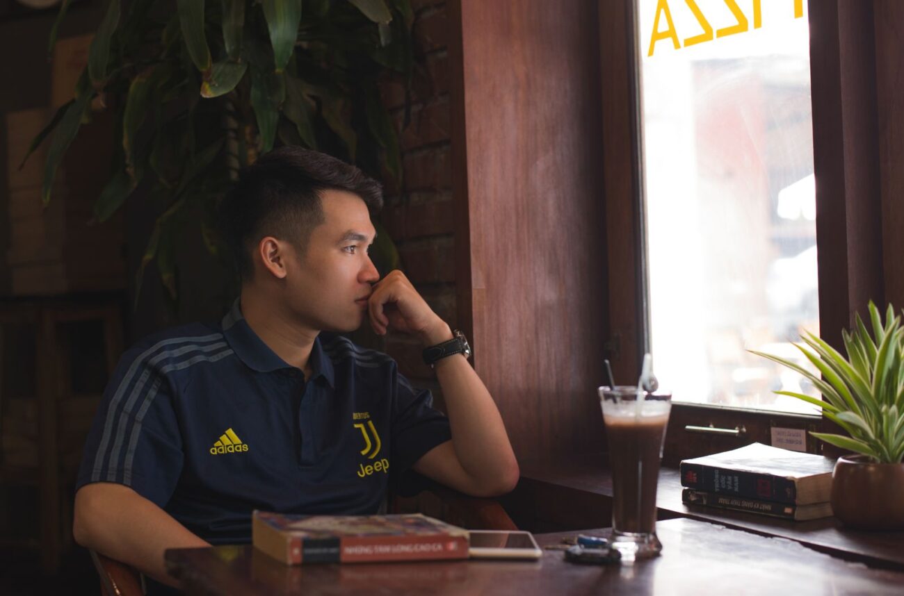 A man sitting alone by a cafe window with a coffee, keeping his plans to himself Image title: keep-goals-to-yourself