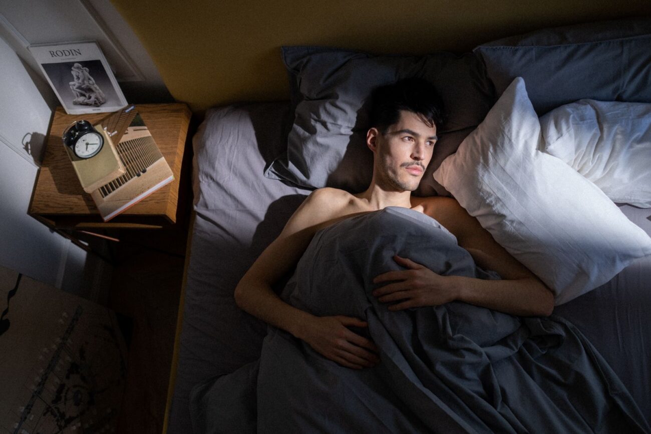 An adult lying awake in bed by an alarm clock, slow to start the morning