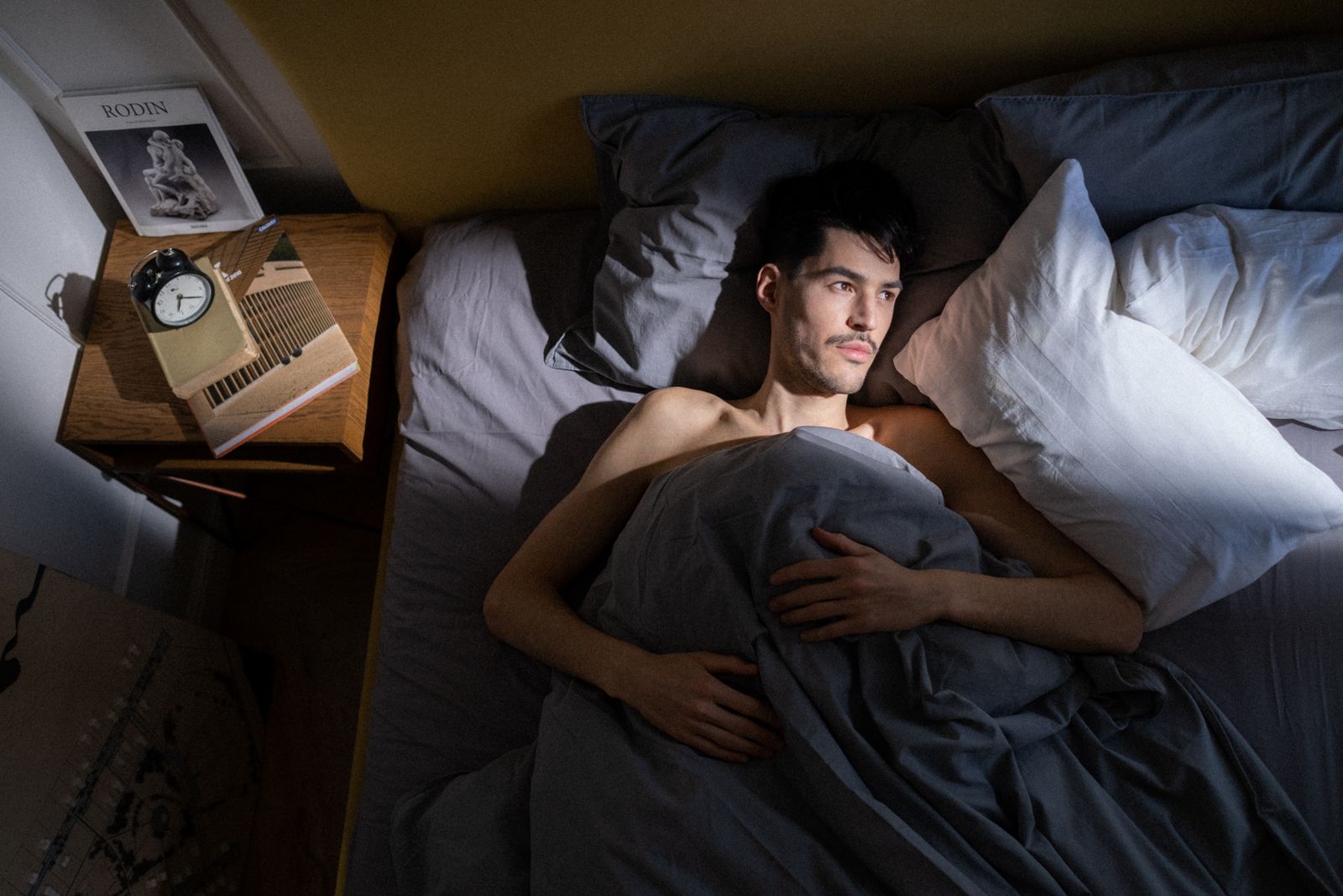 An adult lying awake in bed by an alarm clock, slow to start the morning