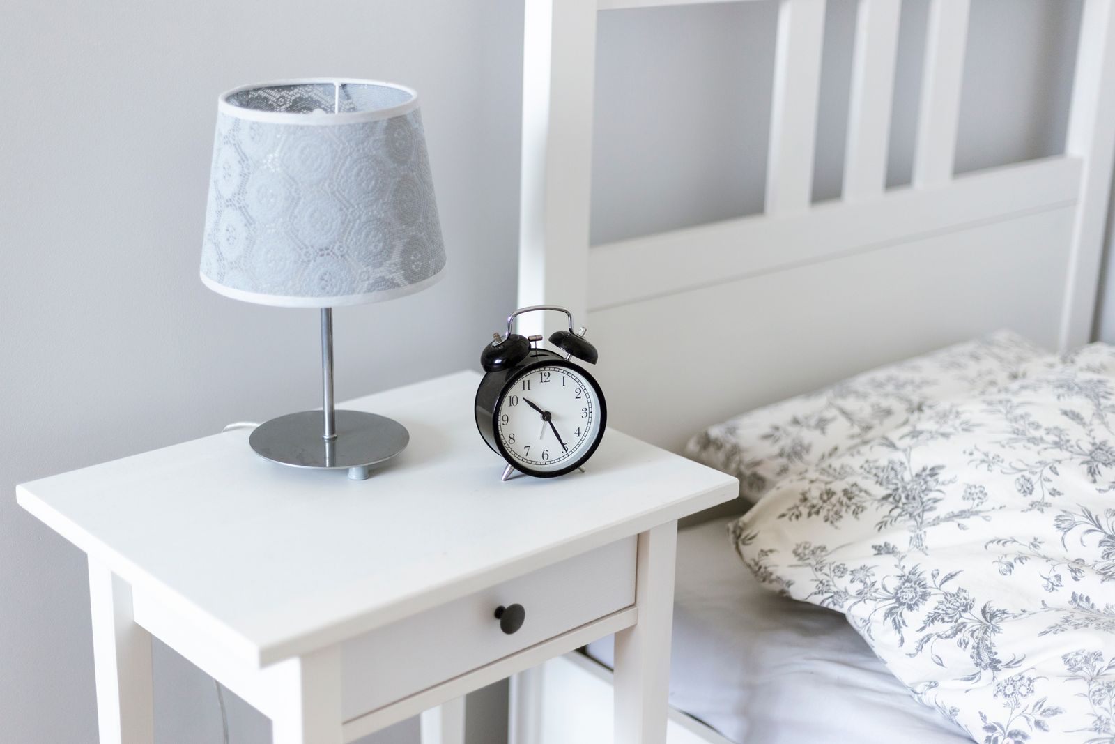 An alarm clock on a bedside table next to a bed, set for an early start