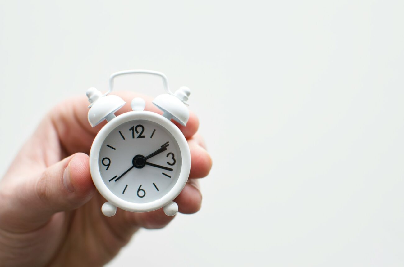 A hand holding a small alarm clock, time passing on a task