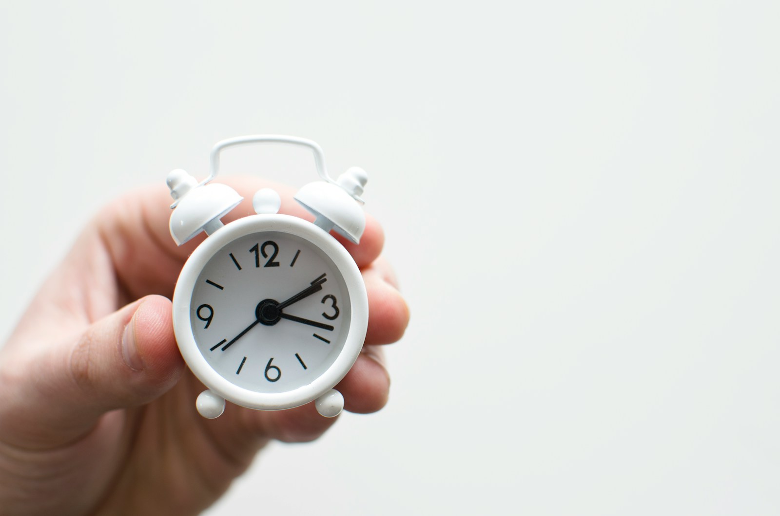 A hand holding a small alarm clock, time passing on a task
