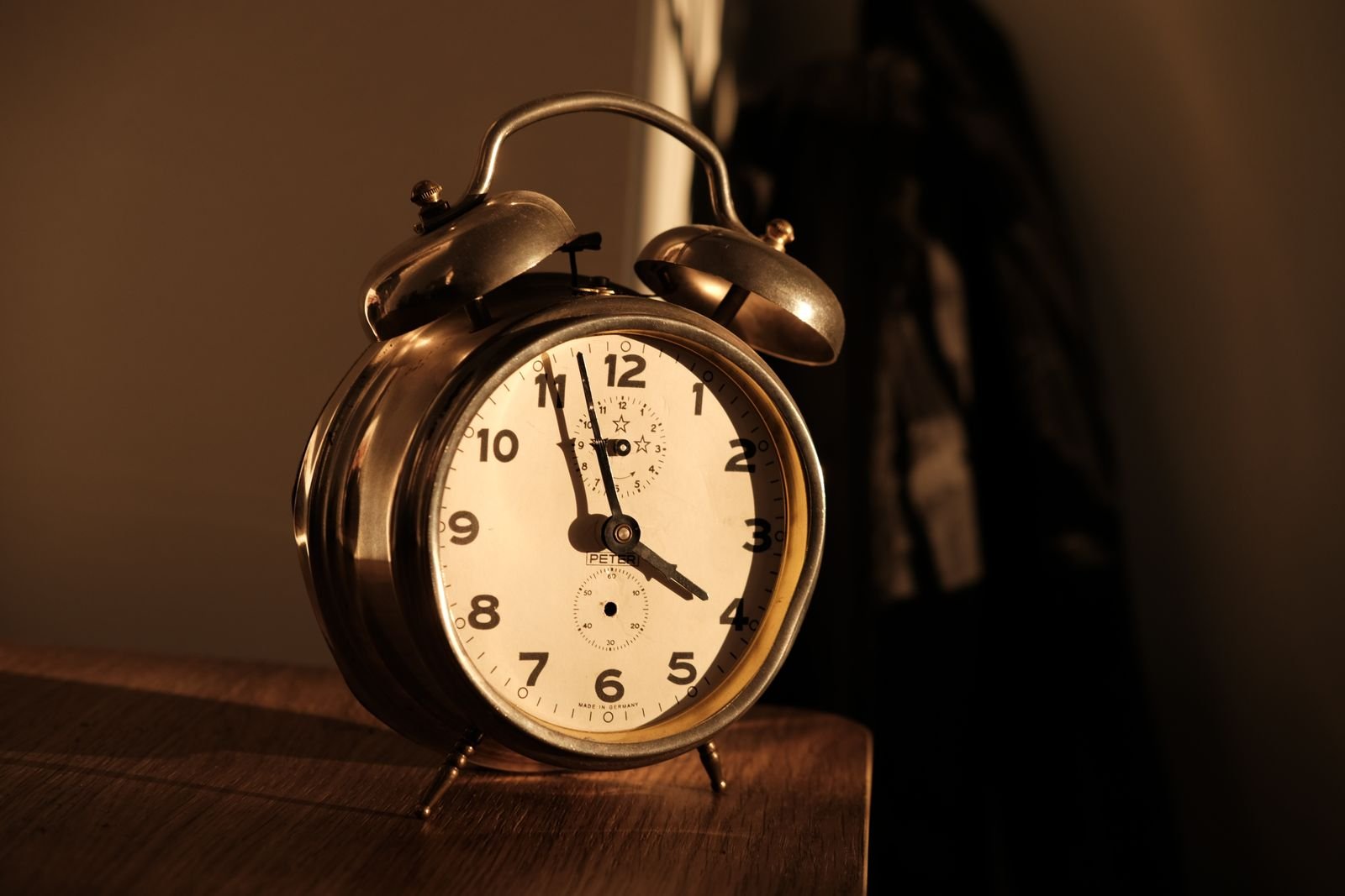 An old-style alarm clock on a wooden table in dim morning light