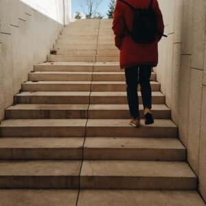 A person seen from behind climbing a wide staircase upward toward an open sky