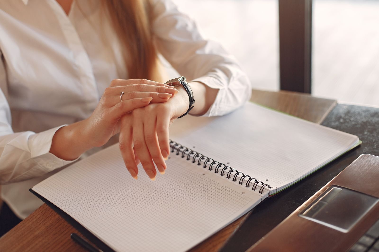 A person checking their watch next to an open notebook at a desk