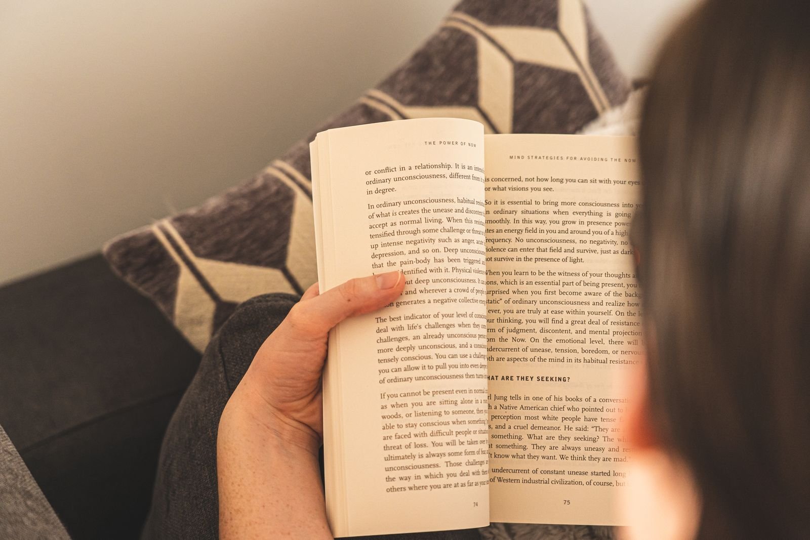 A person reading an open book on a couch at home