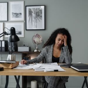 A person sitting at a desk with papers, hand to their head, looking mentally tired